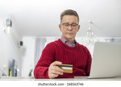 Mature Man Using Credit Card And Laptop To Shop Online At Home