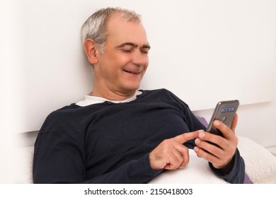 Mature Man Using Mobile Phone In Bed