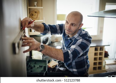 Mature man using a spirit level and marking the wall with a pencil in his kitchen. - Powered by Shutterstock