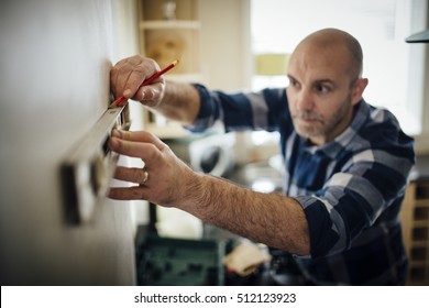 Mature man using a spirit level and marking the wall with a pencil in his kitchen. - Powered by Shutterstock