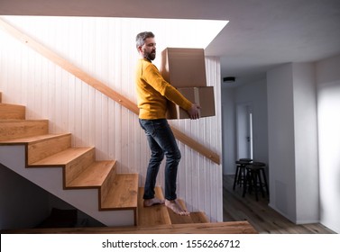 Mature Man Walking Down Stairs In House, Holding Moving Boxes.