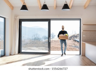 Mature Man Walking In Unfurnished House, Holding A Moving Box.