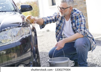 Mature Man Washing His Car With Soapy Sponge In Driveway