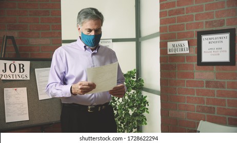 A Mature Man Wearing A Mask Because Of COVID19 Mandates In An Unemployment Office Looking At The Application For Benefits He Is To Complete.