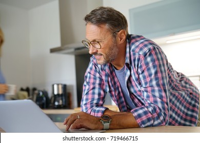 Mature Man Websurfing With Laptop In Home Kitchen