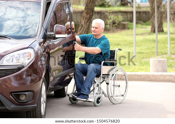 Mature\
man in wheelchair opening door of his van\
outdoors
