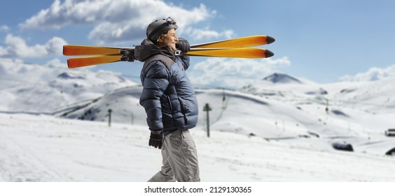 Mature man in a winter jacket walking and carrying skiis on a snowy mountain