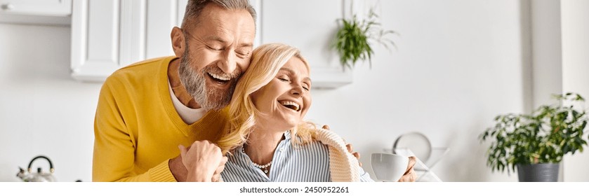 A mature man and woman in homewear share a joyful moment as they laugh together in a cozy kitchen at home. - Powered by Shutterstock