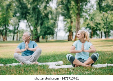 mature man and woman sitting in lotus poses with folded hands and looking away in park