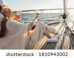 Mature man and woman wrapped in plaid on yacht deck and drinking wine. Senior couple holding glasses of wine on sailbot.