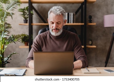 Mature man working on laptop while sitting at his working place - Shutterstock ID 1753400705