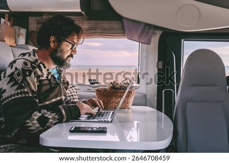 Mature man working remotely from inside a camper van, focused on his laptop while enjoying the freedom of travel. Digital nomad lifestyle, technology on the road, independence and modern remote work