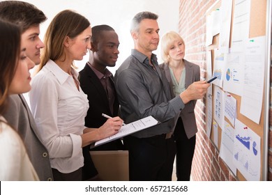 Mature Manager Analyzing The Graph With His Colleague Attached On Bulletin Board - Powered by Shutterstock