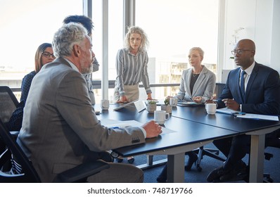 Mature Manager Talking To A Diverse Team Of Employees During A Meeting Around A Table In A Modern Boardroom