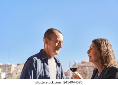 Mature married couple at drinking a glass of wine at balcony over blue sky with copy space - Powered by Shutterstock