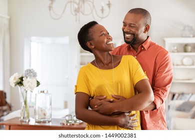 Mature married couple embracing in living room while looking at each other. Newly wed african couple in love hugging at home. Romantic husband with beautiful wife in love at home with copy space.