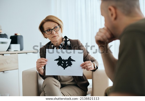 Mature mental health professional using Rorschach\
inkblot test to assess psychological condition of military man in\
her office. 