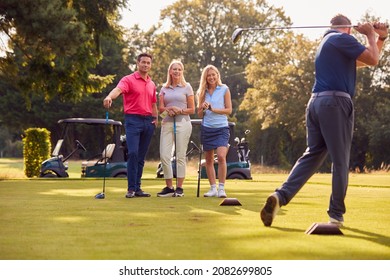 Mature And Mid Adult Couples Standing By Golf Buggy Watching Man Hit Tee Shot