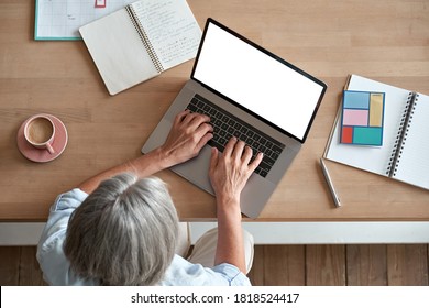 Mature Middle Aged Business Woman Using Laptop Computer Sitting At Workplace Desk. Senior Older Lady, 60s Grey-haired Businesswoman Working At Table Typing On Pc At Home Or From Office, Top View.