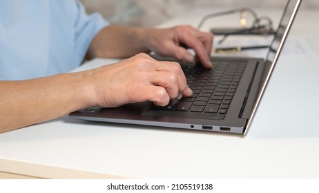 Mature Middle Aged Woman Using Laptop Works On The Computer While Sitting At The Table. Senior Job Seeker Looking For A Job Online. Hands Close-up, Typing.