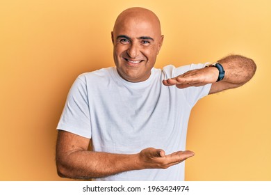 Mature Middle East Man Wearing Casual White Tshirt Gesturing With Hands Showing Big And Large Size Sign, Measure Symbol. Smiling Looking At The Camera. Measuring Concept. 