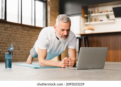 Mature middle-aged athlete man standing in plank position in sporty clothes on fitness mat, watching video training tutorial online, vlogging and blogging at home on lockdown - Powered by Shutterstock