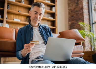 Mature middle-aged caucasian businessman freelancer ceo boss it specialist using credit card for online payment transactions cashback shopping e-banking e-commerce on laptop in office