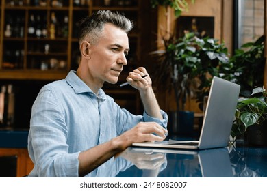 Mature middle-aged caucasian writer author writing novel book, businessman freelancer working remotely, e-learning using laptop in cafe restaurant - Powered by Shutterstock