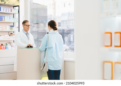Mature middle-aged male caucasian chemist pharmacist druggist explaining advising drugs, painkillers, antibiotics, consulting female customer client buyer in pharmacy drugstore