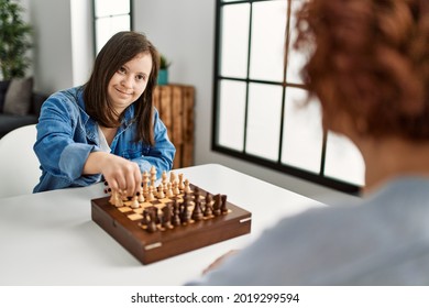 Mature Mother And Down Syndrome Daughter Playing Chess Boardgame At Home