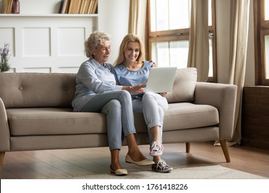 Mature mother grown up daughter sit on couch in living room hold on lap pc looking at screen watching movie film, using device make video call, shopping via e-commerce website, girl teach mom concept - Powered by Shutterstock