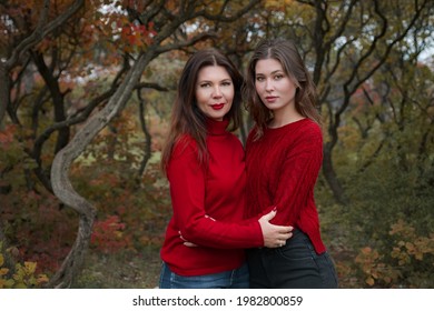 Mature Mother Hugging With Her Teen Daughter Outdoor In Nature On Autumn Day. Fall Fashion, Warm Red Sweaters. Walking In Autumn Forest