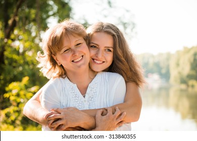 Mature mother hugging with her teen daughter outdoor in nature on sunny day