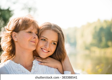 Mature mother hugging with her teen daughter outdoor in nature on sunny day