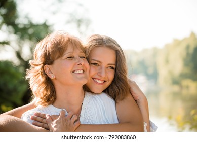 maduro mãe abraços com ela teen filha ao ar livre no natureza no ensolarado dia