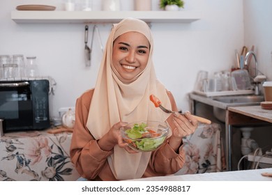 Mature muslim islamic woman in hijab mixing preparing cooking vegetable salad in the kitchen. Vegan vegetarian food concept. - Powered by Shutterstock