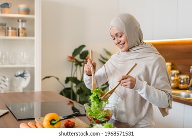 Mature muslim islamic woman wife in hijab mixing preparing cooking vegetable salad in the kitchen. Vegan vegetarian food concept
