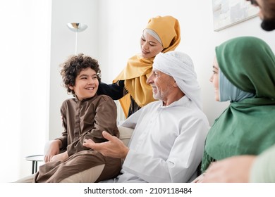 mature muslim man in turban talking to arabian grandson near happy interracial family