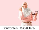 Mature Muslim woman doing makeup on pink background