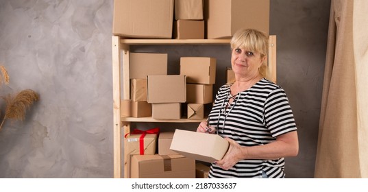 mature older 60s woman retail seller, entrepreneur, clothing store small business owner, woman in warehouse is picking up goods in a box. standing in delivery shipping warehouse, portrait. banner