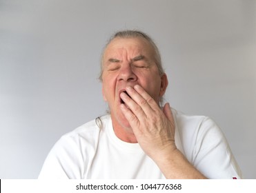 mature older man yawning with hand to mouth. Mouth open and eyes closed, concept, sleep and bored.