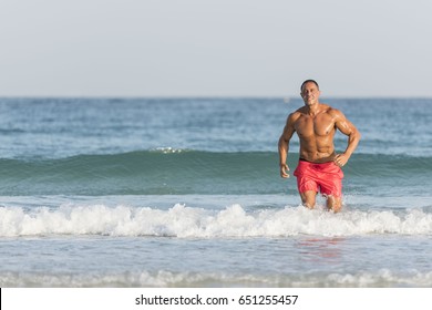 Mature Older Muscular Fit Middle Eastern, Arab Male Running Out Of The Ocean On The Beach, Shirtless, Wearing Red Shorts 