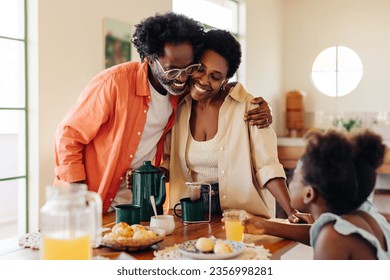 Mature parents smiling and hugging as they enjoy quality time with their daughter at the breakfast table. Black Brazilian family sharing a loving breakfast with delicious pão de queijo and coffee. - Powered by Shutterstock