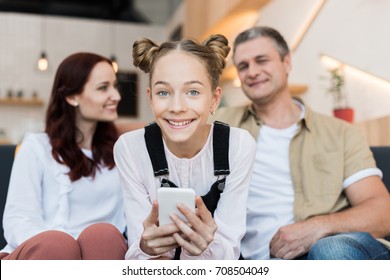 mature parents and teen girl with smartphone in cafe