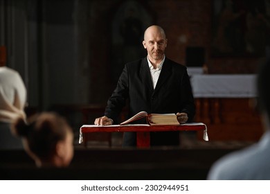Mature pastor reading Bible for believers while standing at altar in church