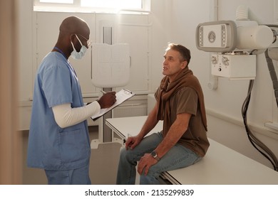 Mature Patient Telling His Name And Other Data To Doctor With Pen And Medical Form Before Examination In Radiologist Office