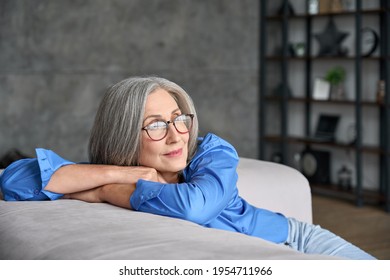 Mature peaceful 60s middle age lady sitting relaxing at home. Senior elder serene woman in glasses looking at window thinking of positive vision, dreaming of future and enjoying wellbeing. - Powered by Shutterstock