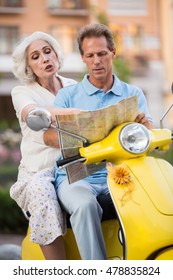 Mature People Sitting On Scooter. Man With Map Beside Woman. We Should Turn Here. I Don't Know This Town.