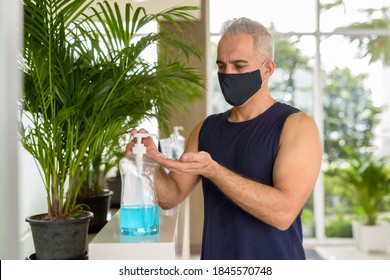 Mature Persian man with mask using hand sanitizer while social distancing at the gym - Powered by Shutterstock