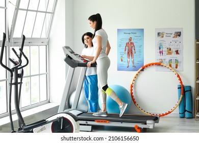 Mature physiotherapist working with young woman on treadmill in rehabilitation center - Powered by Shutterstock